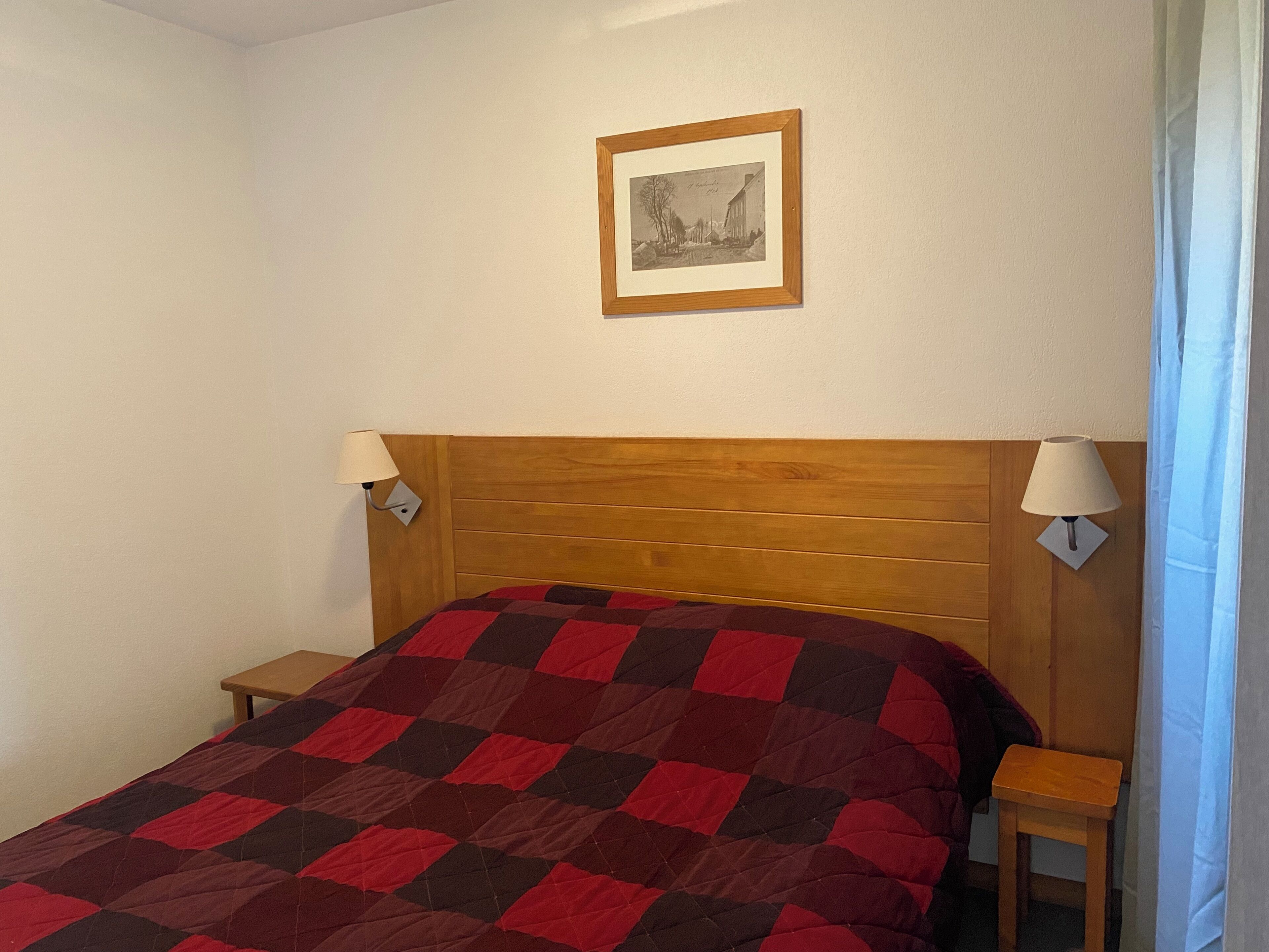 Ein Schlafzimmer mit einem Holzkopfteil, einer karierten Bettdecke, zwei Nachttischen und einem gerahmten Bild an der Wand.