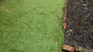 Un patio trasero con césped verde, un muro de ladrillo y un pequeño jardín.