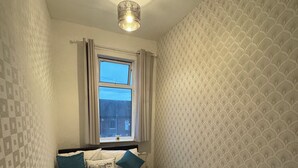 Un dormitorio pequeño y ordenado con una cama individual, una ventana con cortinas y papel tapiz estampado.