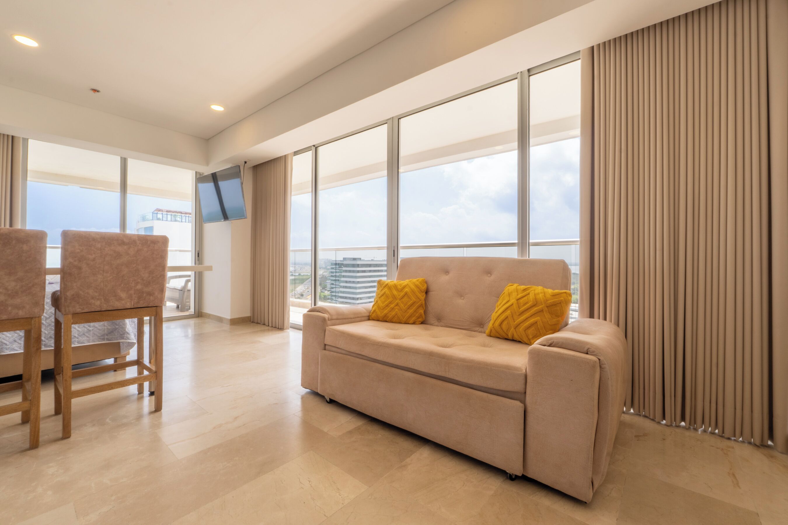Una sala de estar moderna con sofá, sillones, televisor de pantalla plana y grandes ventanales con vistas a la ciudad.