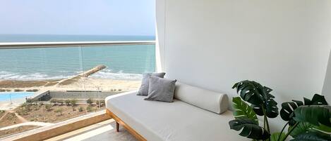 A balcony with a view of the ocean and a modern sofa with cushions.