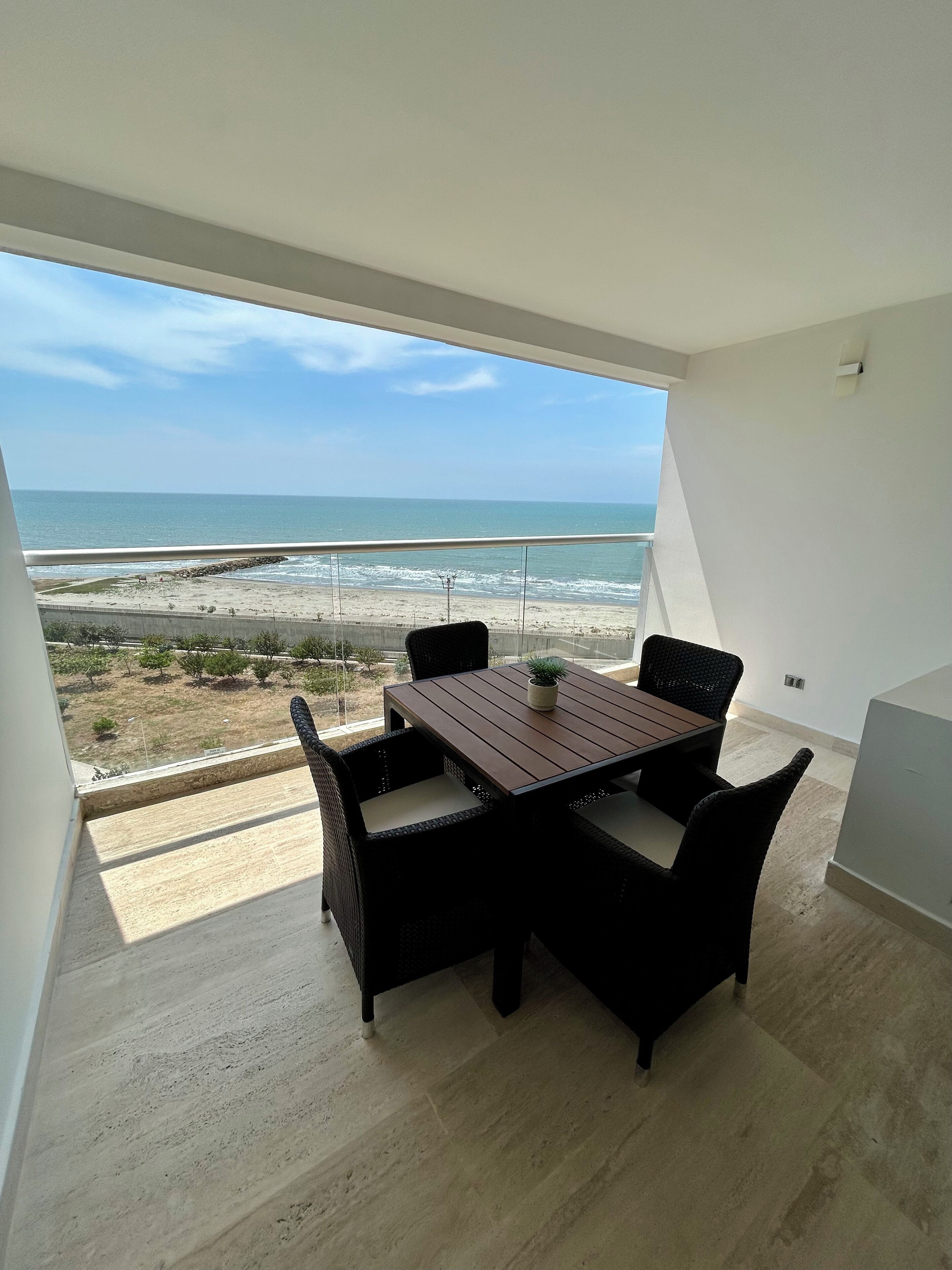 A balcony with a wooden table and chairs, overlooking a beach and ocean.