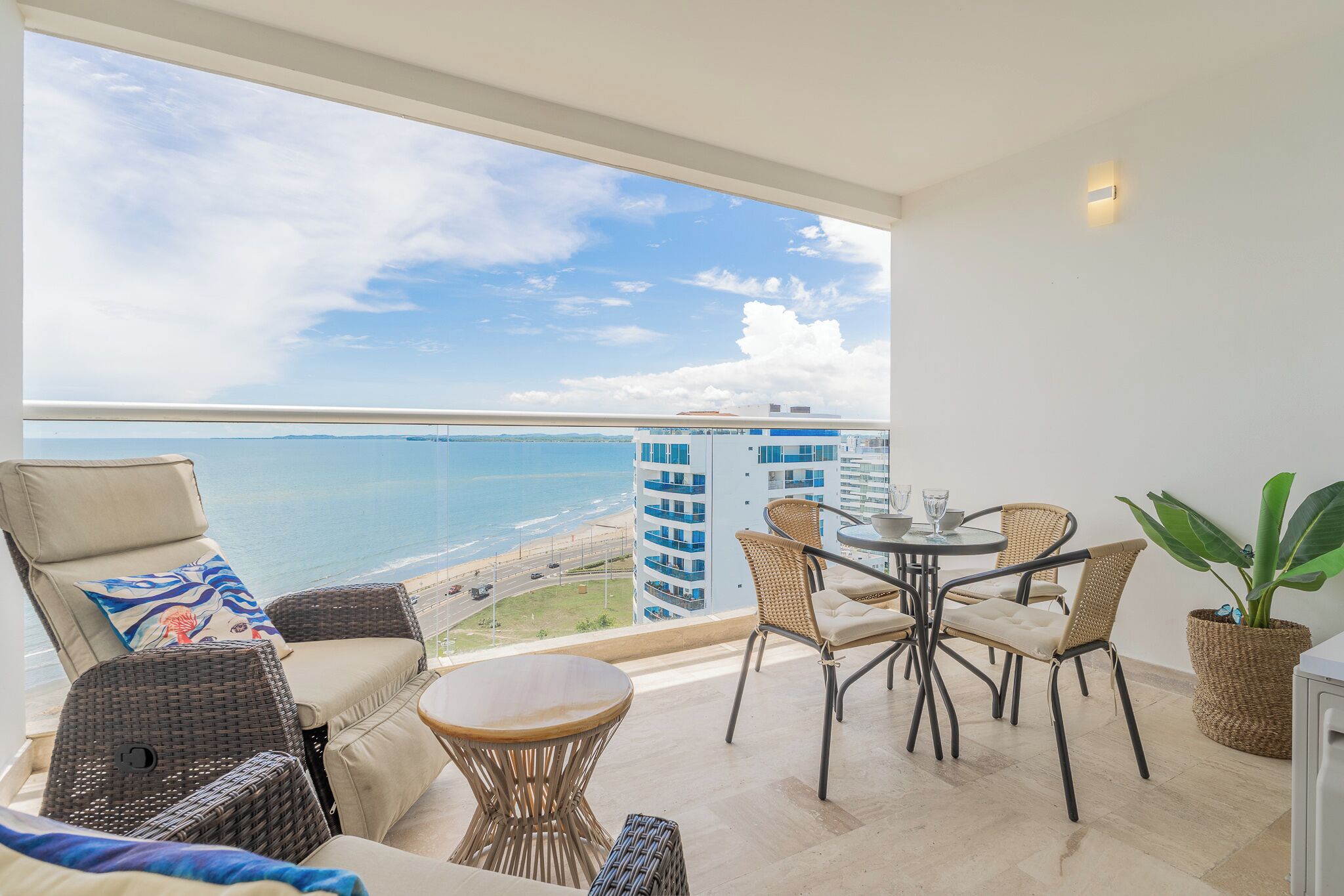Een balkon met uitzicht op de oceaan, rieten meubels en een potplant.