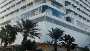 A tall, modern hotel with a curved facade, multiple balconies, and a central entrance with palm trees in the foreground.