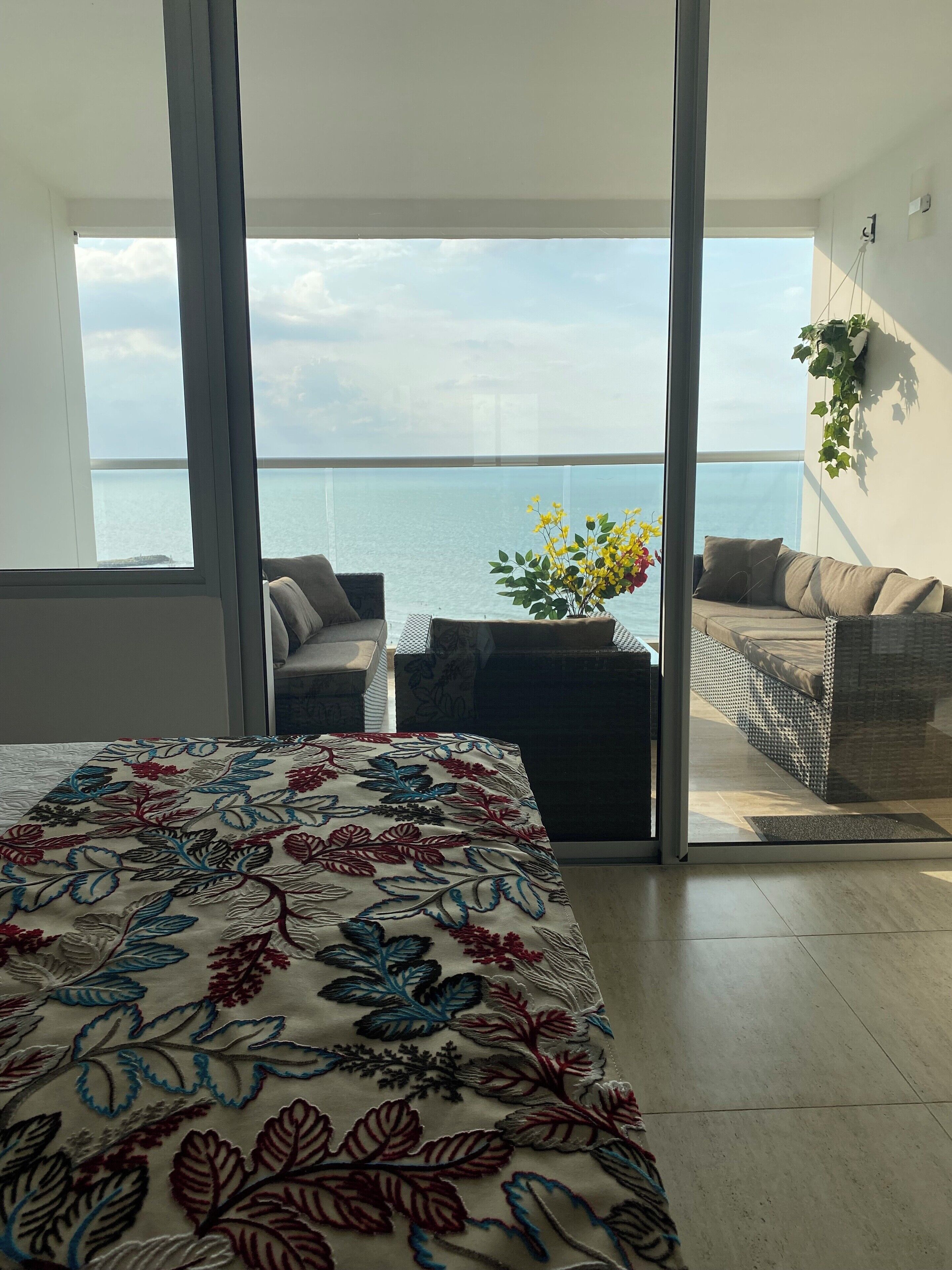 A balcony with a view of the sea, a bed with a floral bedspread, and a sofa with cushions.