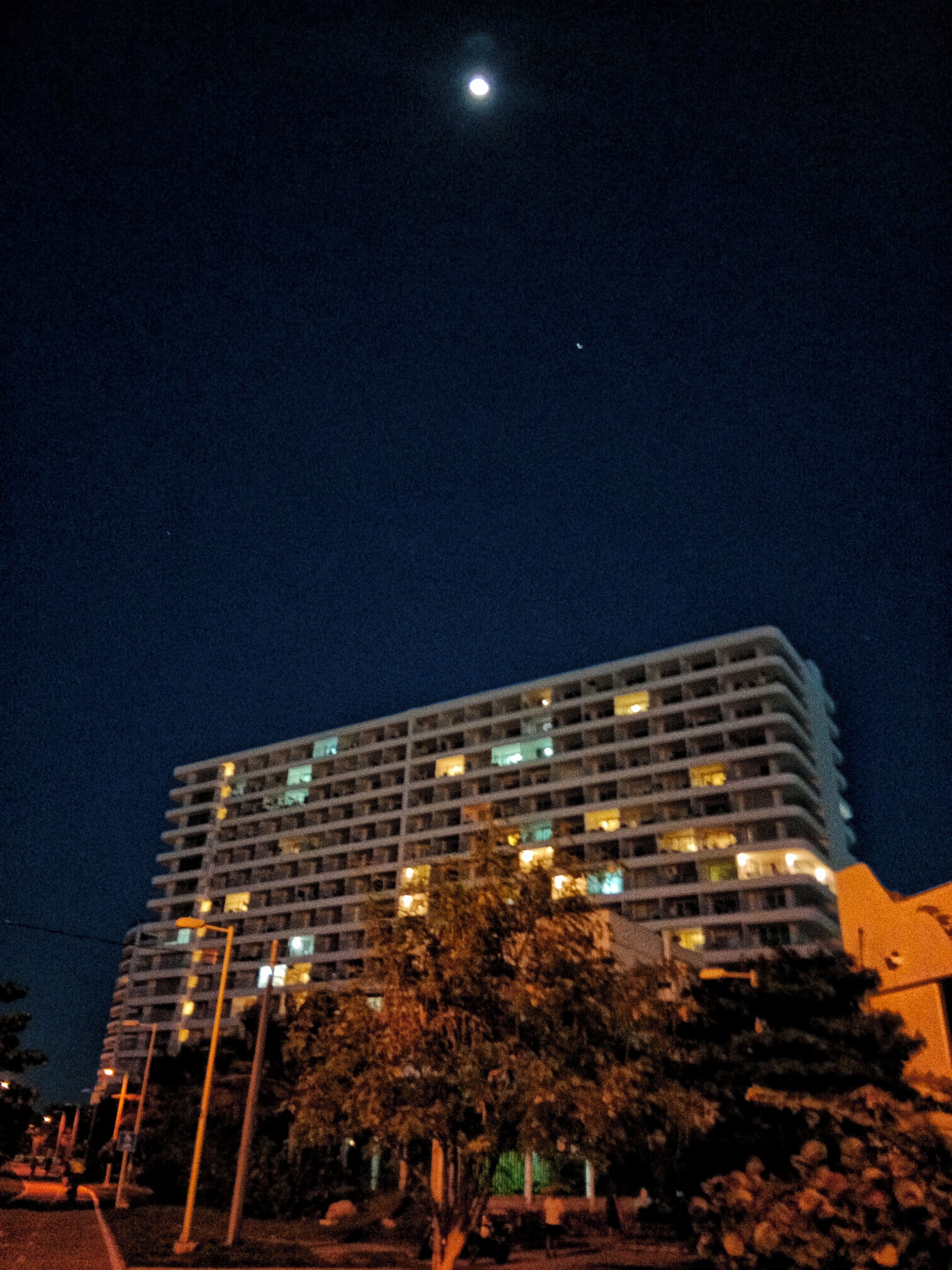 A multi-story building with illuminated windows at night, surrounded by trees and street lamps.