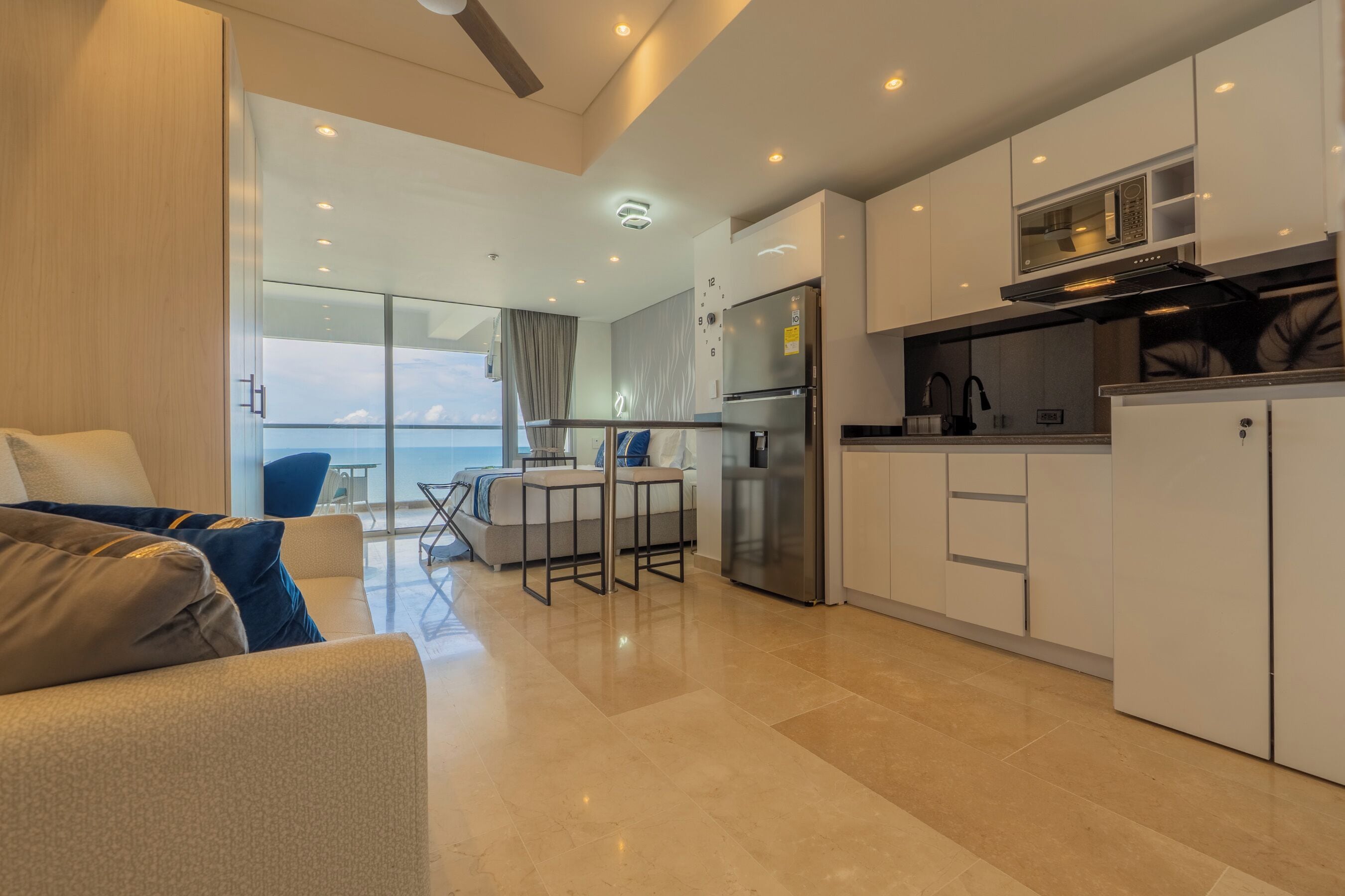 Una cocina moderna con armarios blancos, un refrigerador de acero inoxidable y una zona de comedor con mesa y sillas.