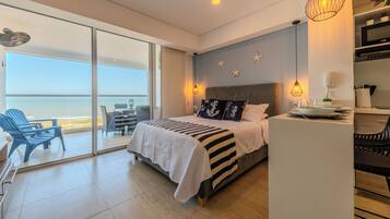 Une chambre moderne avec un grand lit, un balcon offrant une vue sur la mer et un petit coin cuisine.