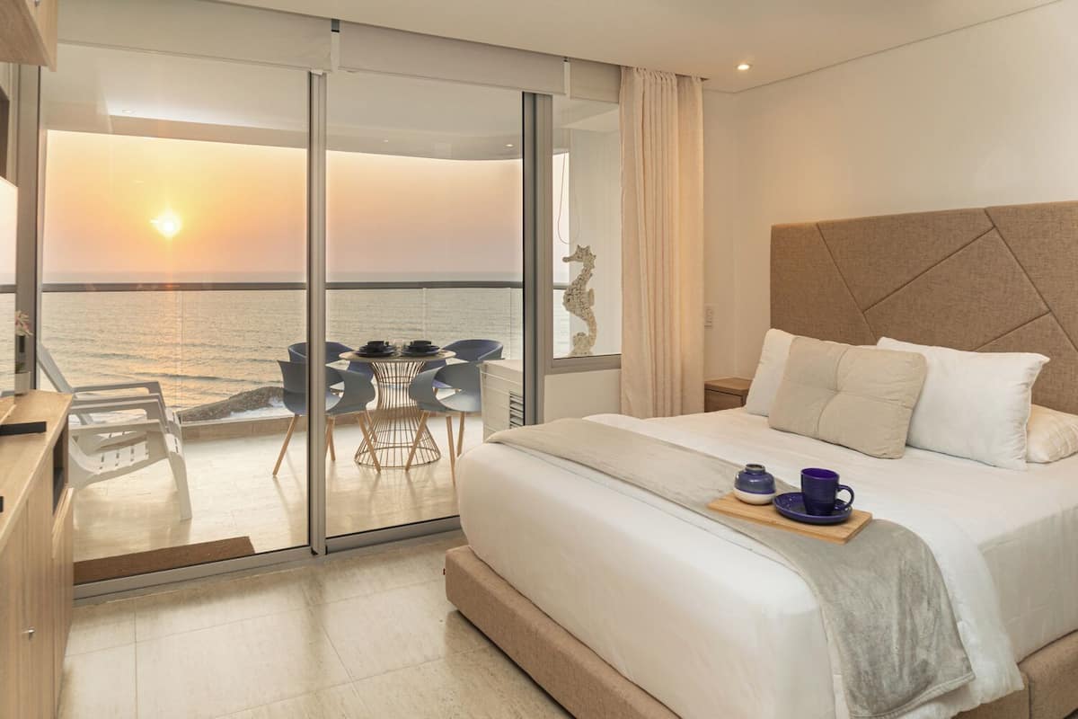 A hotel room with a bed, a breakfast tray, a table with chairs, and a view of the ocean.