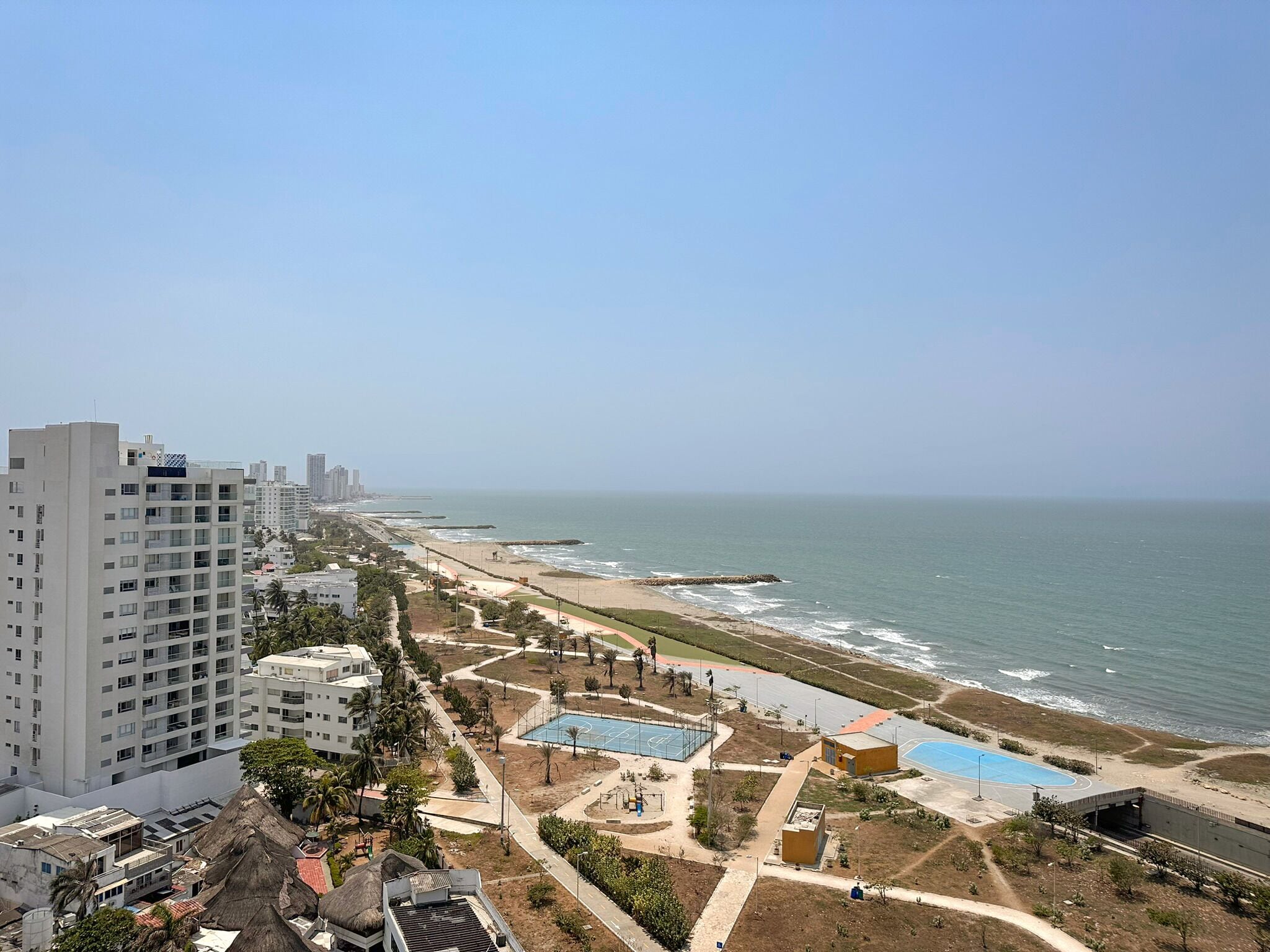 A coastal resort with a beach, a pool, and high-rise buildings in the background.