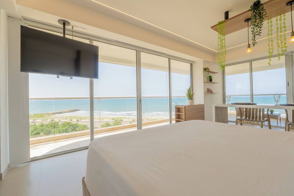 A bedroom with a large bed, a TV, and a view of the ocean.