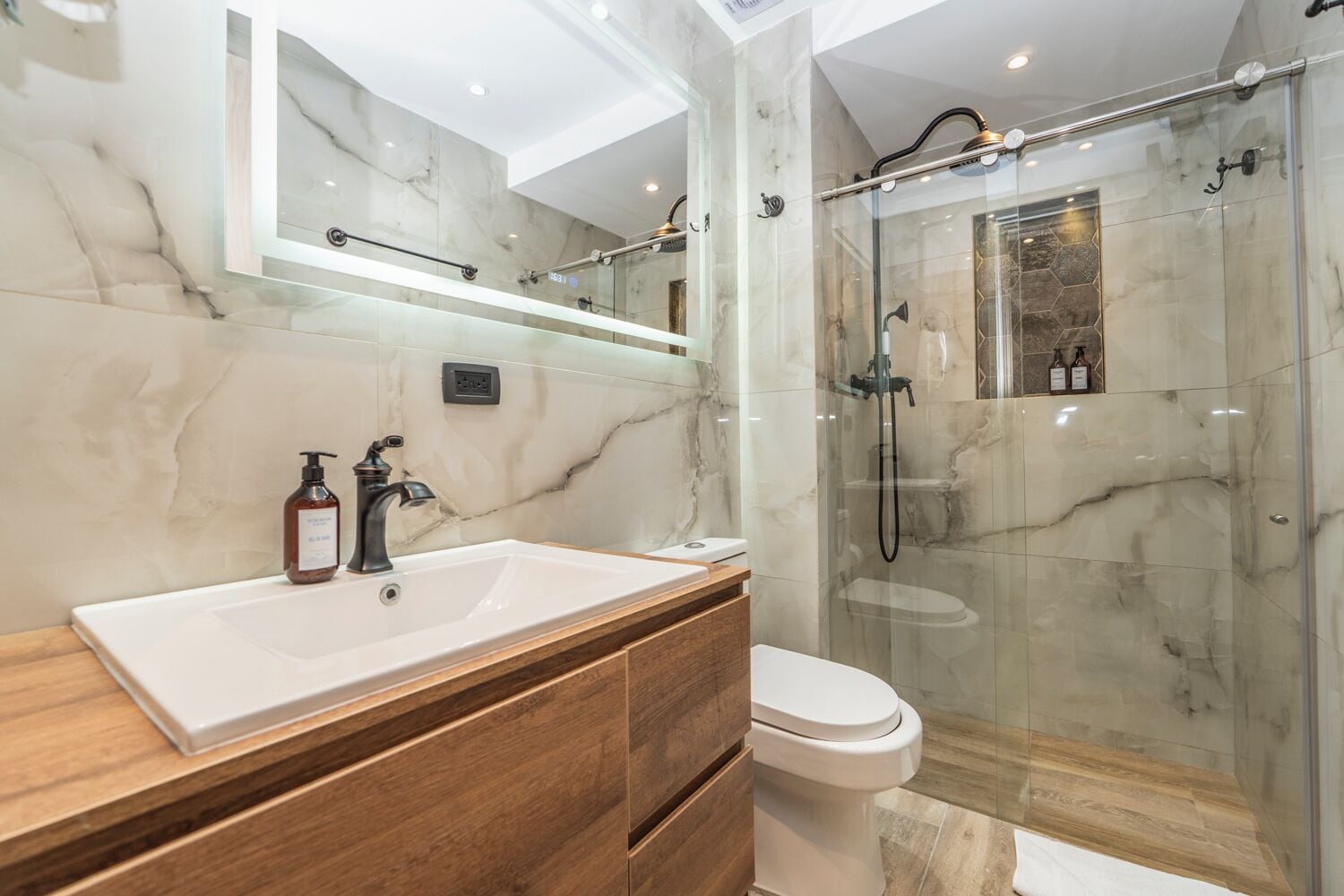 A modern bathroom with a marble sink, a toilet, and a glass-enclosed shower area.