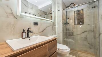 A modern bathroom with a marble sink, a toilet, and a glass-enclosed shower area.
