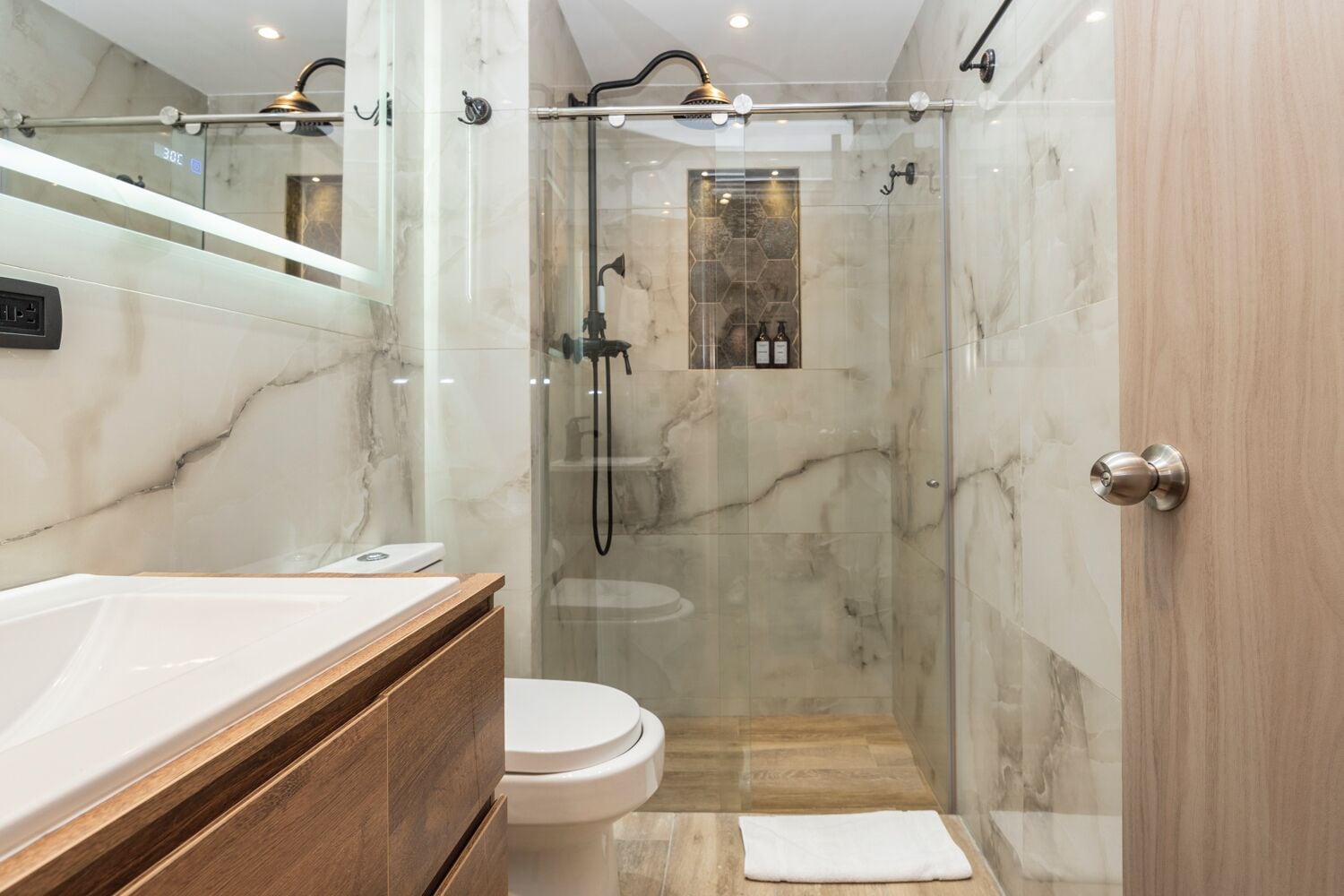 A modern bathroom with a glass-enclosed shower, a wooden vanity, and a marble backsplash.