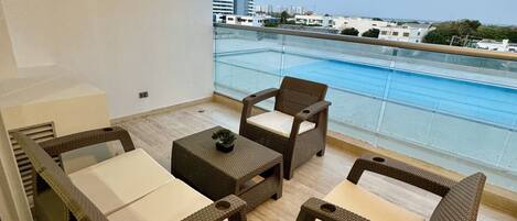 A balcony with wicker furniture, a small table, and a view of the sea and buildings.