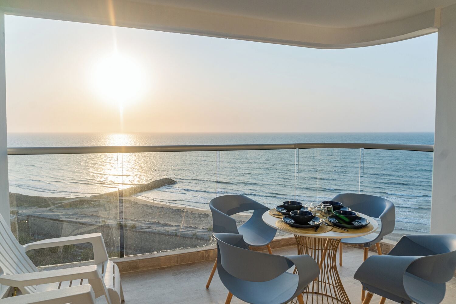 A balcony with a table set for dining, overlooking a beach and the ocean.