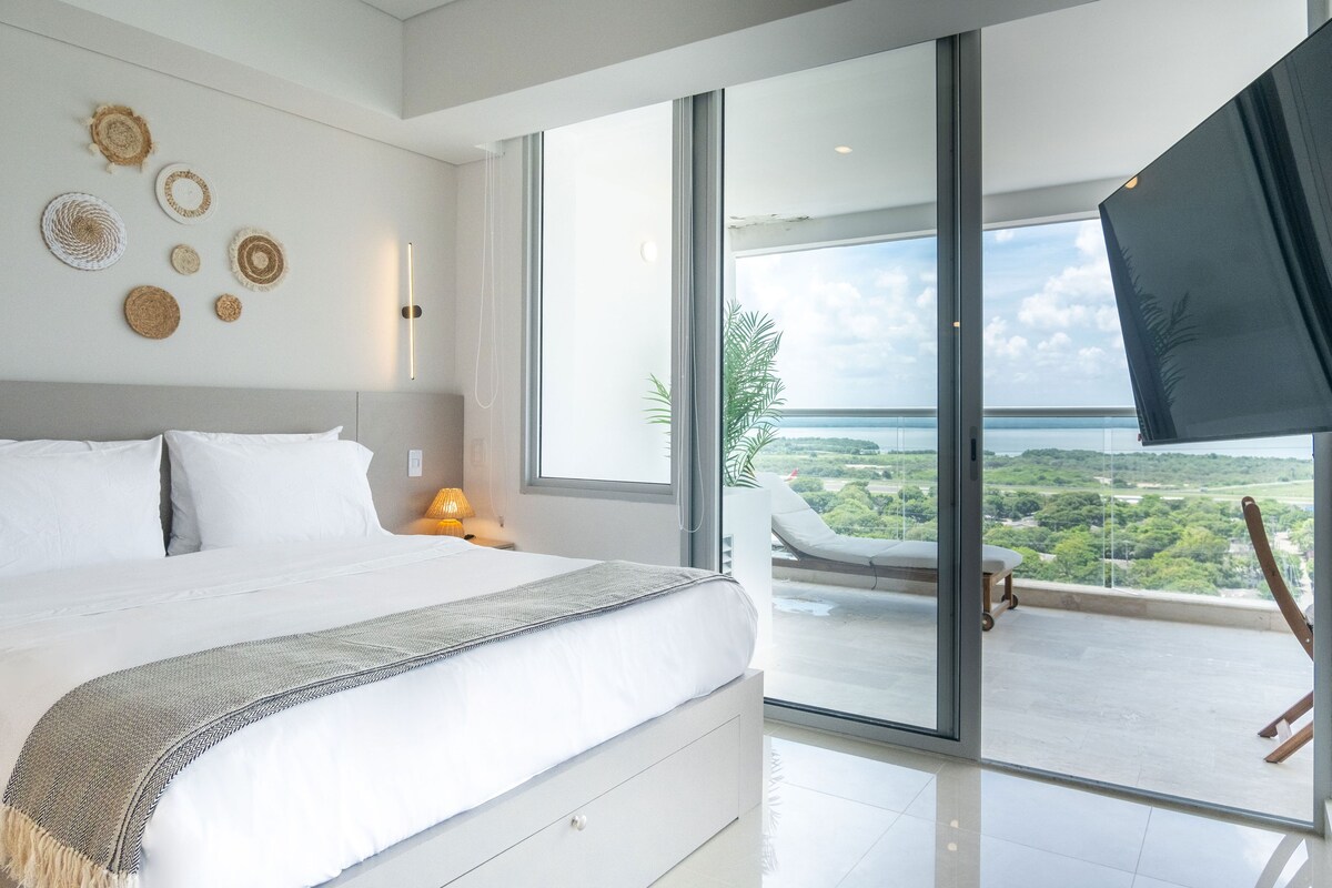 A modern bedroom with a large bed, a balcony with a view, and decorative wall art.