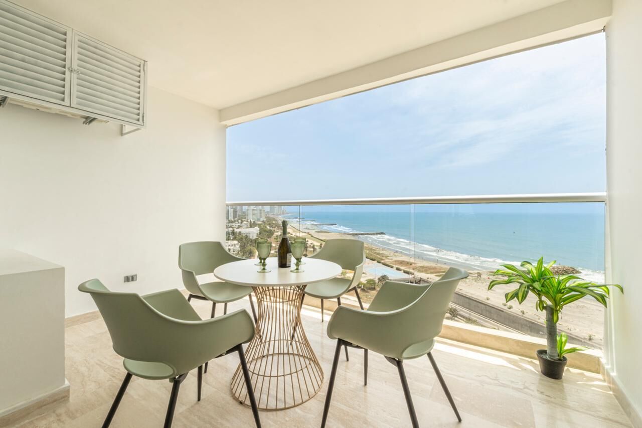 A balcony with a view of the ocean, a round table with chairs, and a potted plant.