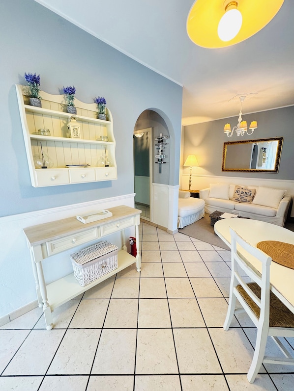 A modern living room with a white sofa, a coffee table, a console table with storage, a mirror, and a door with directional signs. - Cozy apartment surrounded by nature with a beautiful lake view.  (Torri del Benaco)