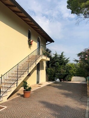A building with a staircase leading to a balcony, surrounded by greenery and a paved courtyard. - Cozy apartment surrounded by nature with a beautiful lake view.  (Torri del Benaco)
