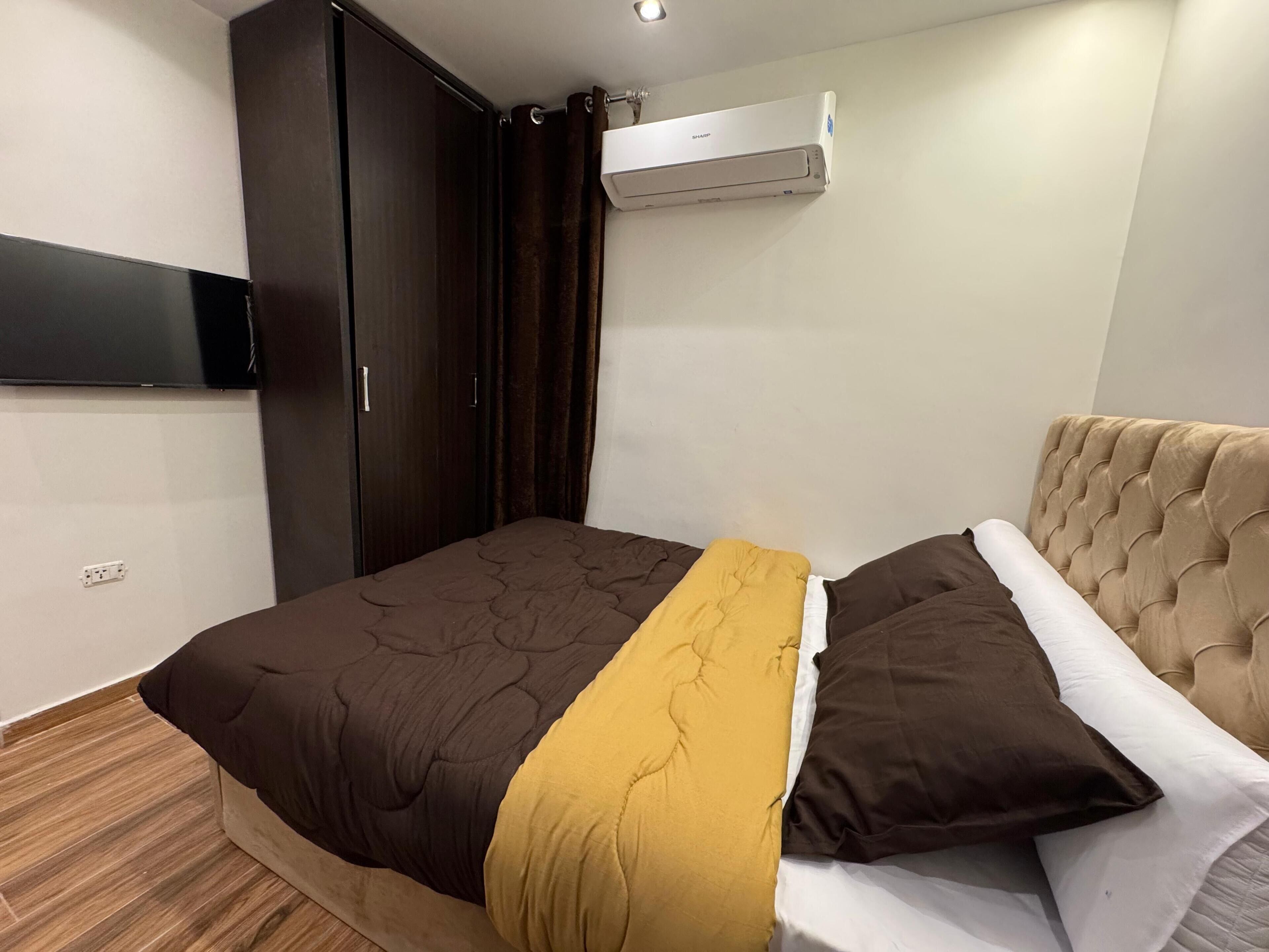 A bedroom with a bed, a wardrobe, an air conditioning unit, and a television mounted on the wall.