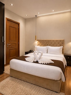 A hotel room with a large bed, a wooden door, a nightstand, and a wall-mounted light fixture. - New White Pyramids Inn (Giza)
