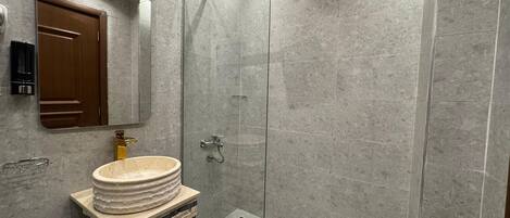 A modern bathroom with a glass-enclosed shower, a marble sink, and a wooden door.