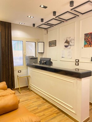 Un mostrador de recepción con una impresora, una ventana con cortinas, una pared con cuadros enmarcados y un suelo de madera.