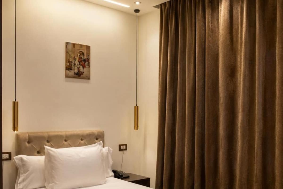 A modern hotel room with a large bed, a bedside table, a wall-mounted lamp, and a painting.