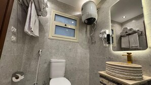 A modern bathroom with a toilet, a sink with a stone-like countertop, a hairdryer, and towels hanging on a rack. - New White Pyramids Inn (Giza)