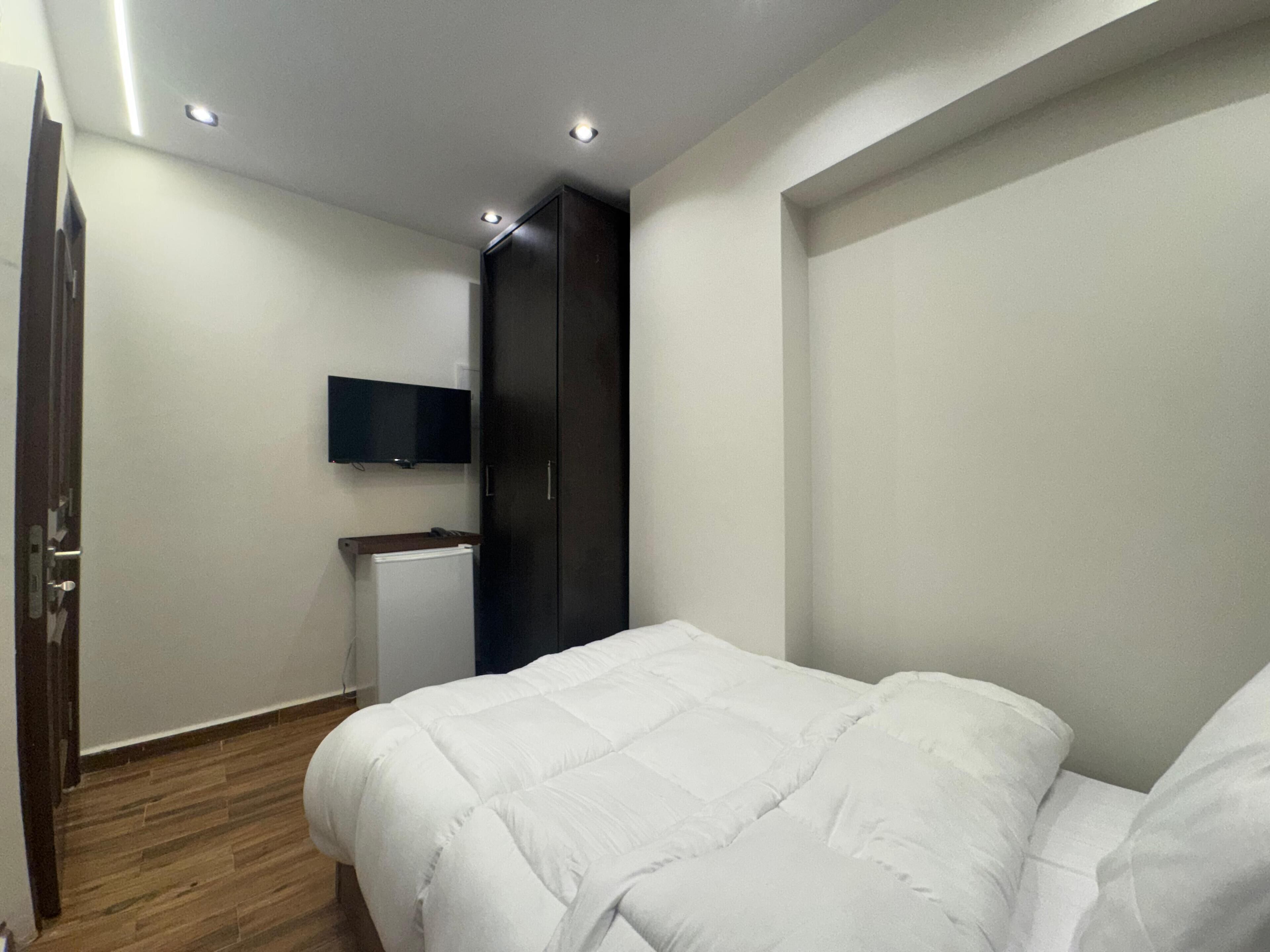 A bedroom with a bed, a wardrobe, a television, and a radiator.