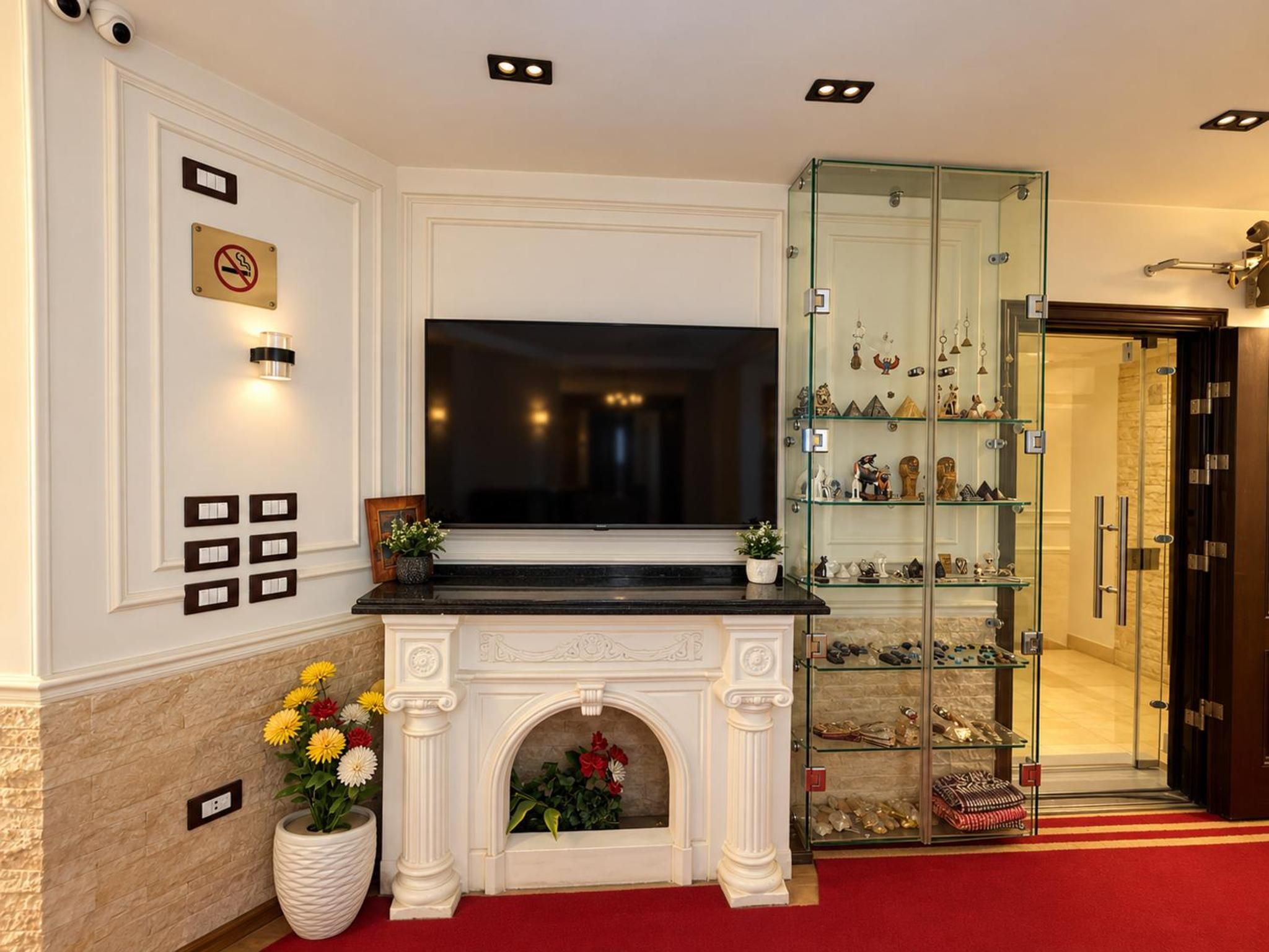 A hotel lobby with a fireplace, a glass display case with decorative items, and a red carpet.