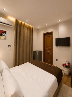 A hotel room with a bed, a television mounted on the wall, a door, and a small cabinet. - New White Pyramids Inn (Giza)