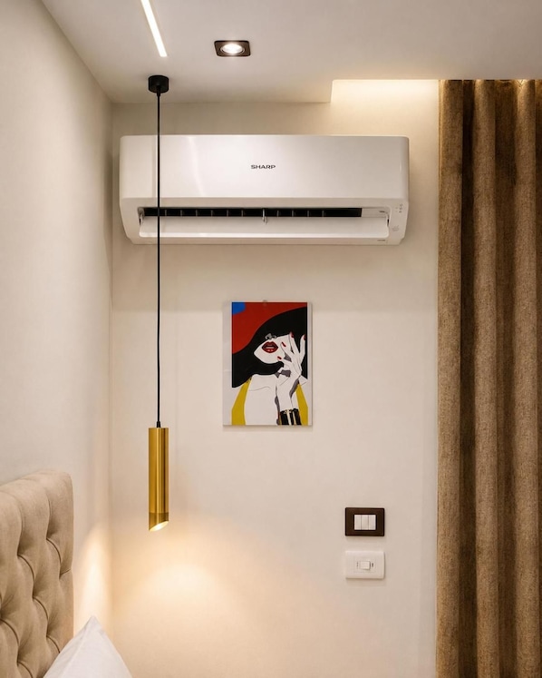 A room with a mounted air conditioner, a pendant light, a framed artwork, and a wall switch. - New White Pyramids Inn (Giza)