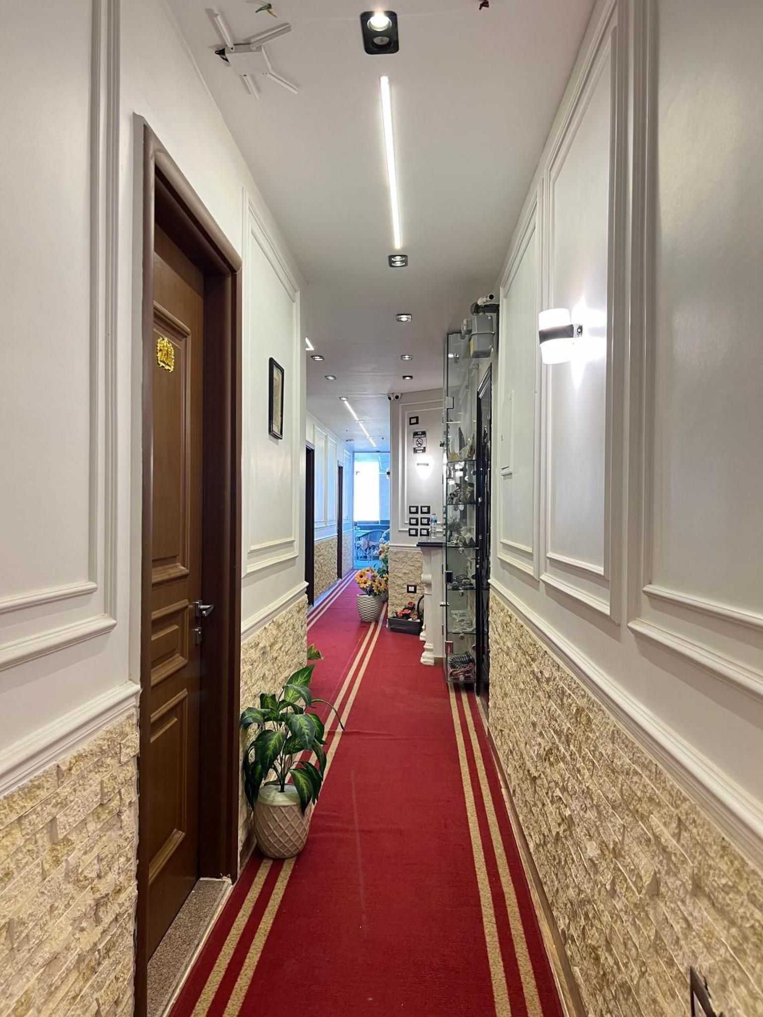 A hotel corridor with a red carpet, stone wall paneling, and a wooden door with a gold emblem.