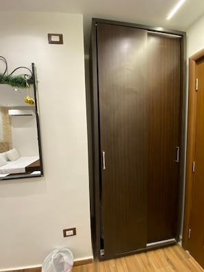 A room with a wooden door, a mirror on the wall, and a small trash bin. - New White Pyramids Inn (Giza)