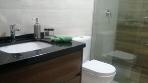 A bathroom with a modern design, featuring a dark wood vanity, a white sink, and a glass shower enclosure. - 1-bedroom apartment in Cochabamba (Cochabamba)