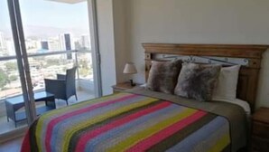 A bedroom with a large bed, a nightstand, a lamp, and a chair. - 1-bedroom apartment in Cochabamba (Cochabamba)