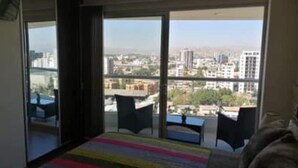 A bedroom with a large window, a bed, and a view of the cityscape. - 1-bedroom apartment in Cochabamba (Cochabamba)