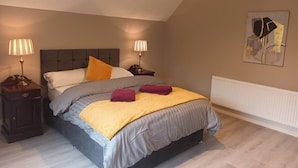 Un dormitorio con una cama, dos mesitas de noche, lámparas, un radiador y una obra de arte en la pared.