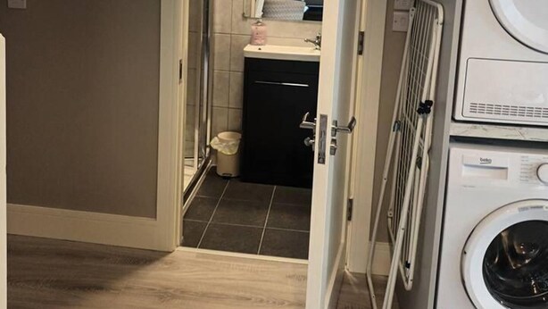 Un lavadero con lavadora y secadora, un lavamanos pequeño y una zona de ducha visible a través de una puerta abierta.