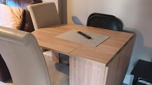 Una pequeña mesa cuadrada de madera con un control remoto encima, rodeada por dos sillas.