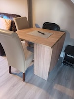 Una pequeña mesa cuadrada de madera con un control remoto encima, rodeada por dos sillas.