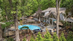 Uma casa com piscina, deck e uma grande árvore em primeiro plano.