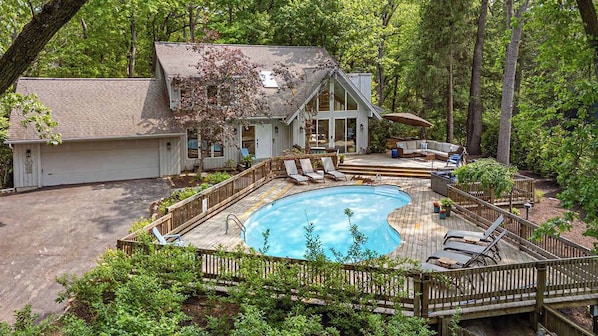 Una casa con piscina, sillas de deck y un espacio de estar cubierto.