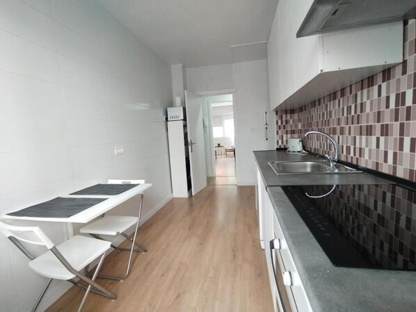 A compact kitchen with white cabinetry, a tiled backsplash, and a stainless steel sink.