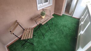 A small balcony with a wooden table, two chairs, and a potted plant.