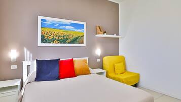 Een slaapkamer met een bed, een gele stoel, een nachtkastje, een wandplank en een schilderij van een zonnebloemenveld.