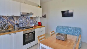 Una cocina moderna con gabinetes blancos, un salpicadero estampado, una estufa a gas y un horno empotrado. Hay una mesa de comedor con sillas y un banco azul estampado.