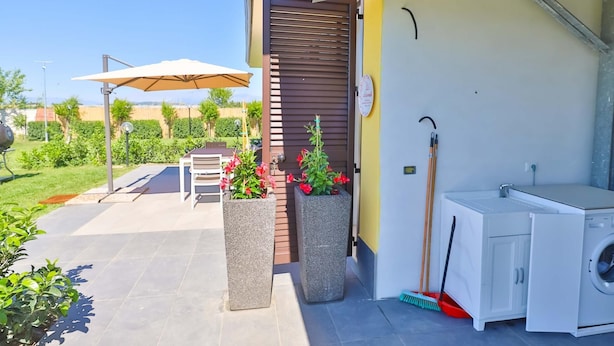 Un patio exterior con una mesa, sillas, una parrilla y plantas en macetas.